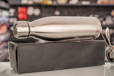 Bir adet metal termos şişesi ve masanın üzerinde bir karton kutu, makro, arka plandaki bar raflarına karşı..
