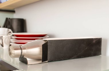 Bir metal termos şişesi, karton kutu ve tabaklar rafta, makro.