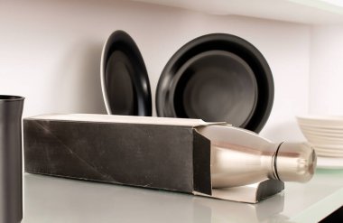 Bir metal termos şişesi, karton kutu ve tabaklar rafta, makro.