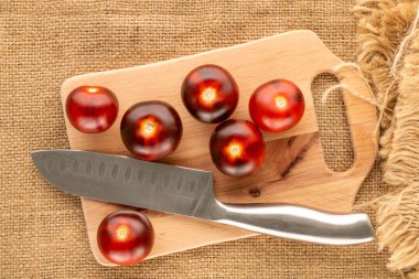 Birkaç organik siyah kiraz domatesli ahşap mutfak tahtası ve jüt kumaş üzerinde bıçak, makro, üst manzara..