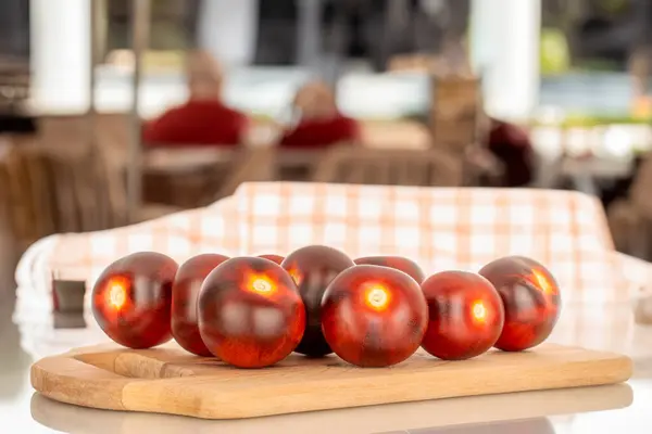 Several ripe black cherry tomatoes on a wooden tray, macro, on the background of a cafe.