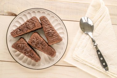 Birkaç parça çikolatalı waffle, seramik tabak ve ahşap masa üzerinde kaşık.