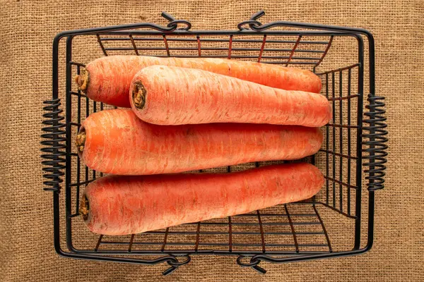 Several ripe carrots in a basket on a jute cloth, macro, top view.