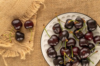 Seramik bir tabakta jüt kumaş, makro, üst görünüm üzerinde birkaç olgun kiraz..