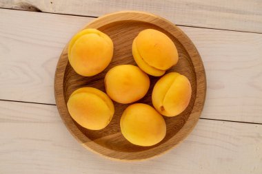 Ahşap bir masanın üzerinde ahşap bir tabakla, makro manzaralı birkaç olgun kayısı..