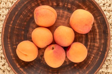 Birkaç sulu kayısı, hasırın üzerinde kil bir tabak, makro, üst görünüm..