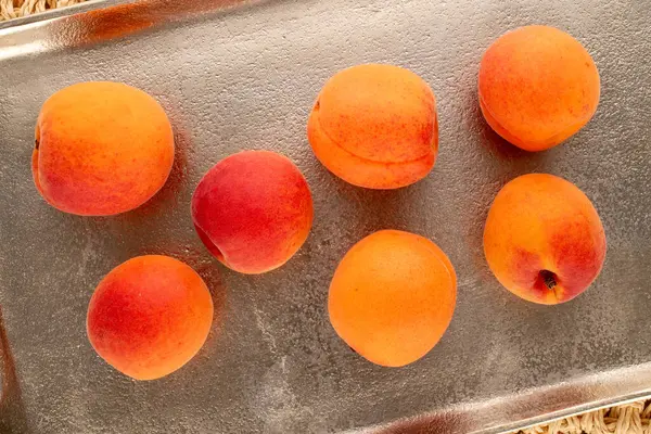 stock image Several juicy apricots with metal tray on straw mat, macro, top view.