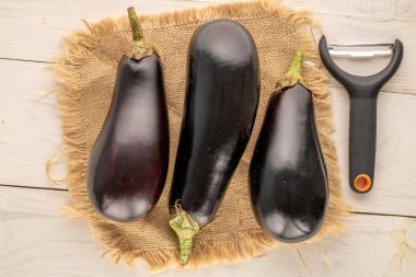 Tahta bir masanın üzerinde jüt peçeteyle üç olgun patlıcan, makro, üst manzara..