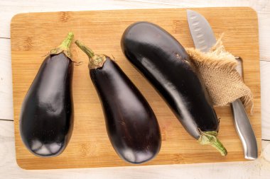 Tahta masa, makro, üst manzara üzerinde bambu kesme tahtasıyla üç olgun patlıcan.