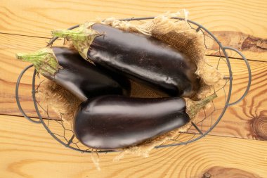 Tahta bir masada sepetin içinde üç olgun patlıcan, makro, üst manzara..