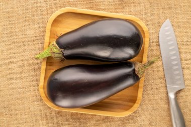 Bambu plakalı iki olgun patlıcan ve jute kumaş üzerinde bıçak, makro, üst görünüm..