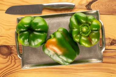 Üç yeşil biber, metal tepsi ve bıçak ile ahşap masa, makro, üst manzara.