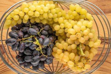 Tahta bir masa, makro, üst manzara üzerinde sepet içinde olgun beyaz ve siyah üzümler..