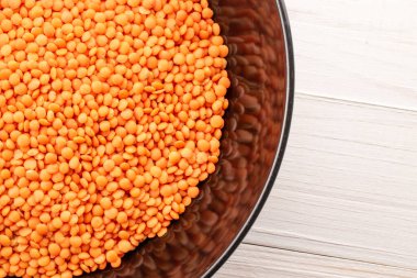 Ahşap bir masada seramik bir tabakta çiğ kırmızı mercimek, makro, üst manzara.