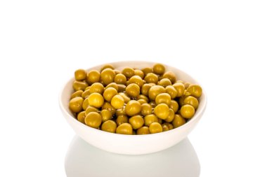 Beyaz seramik bir çanakta konserve yeşil bezelyeler, yakın plan, beyaz arka planda izole edilmiş..