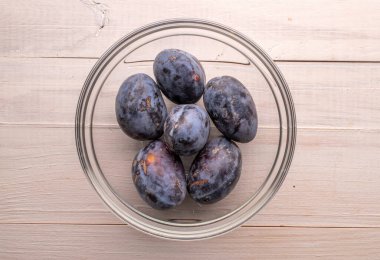 Black ripe plums with household utensils on a wooden table, close-up, top view. clipart