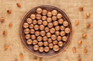 Resim oluşturuldu. Resim oluşturuldu. Kabuklu Macadamia fındıkları, jüt kumaş üzerinde kil plaka, üst manzara..