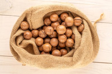 Kabuklu Macadamia fındıkları, ahşap masa üzerinde jüt çanta, üst görünüm.