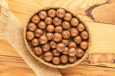 Kabuklu Macadamia fındığı, ahşap masa üzerinde saman tabağı, üst manzara..