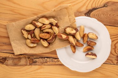 Kabuksuz Brezilya fıstığı beyaz seramik tabak ve kağıt torba ile ahşap masa, yakın çekim, üst görünüm.
