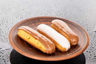 Three eclairs with cream filling on a clay dish on a glass table. clipart