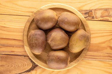 Several ripe kiwis in a wooden plate on a wooden table, close-up, top view. clipart