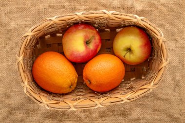 İki tatlı portakal ve iki elma bir sepetin içinde jüt kumaş üzerinde, yakın plan, üst manzara.