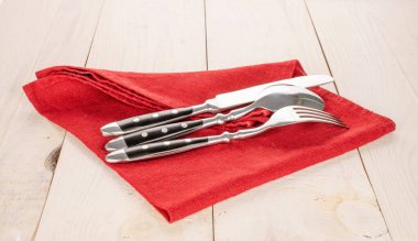 Ahşap bir masanın üzerinde keten peçeteli çatal bıçak takımı, yakın plan..