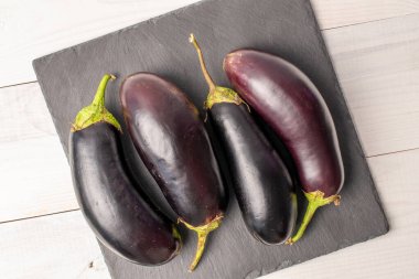 Dört olgun siyah patlıcan, tahta üzerinde, beyaz ahşap bir masada, üst manzara.