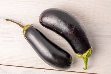 İki olgun mor patlıcan, yakın plan, beyaz ahşap masa, üst manzara.