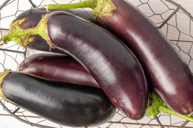 Bir sepetin içinde, beyaz ahşap bir masanın üzerinde, birkaç tane koyu mor patlıcan..