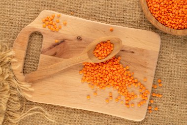 Ahşap kaşıklı kırmızı mercimek ve jüt kumaşlı ahşap mutfak tahtası, yakın çekim, üst manzara..