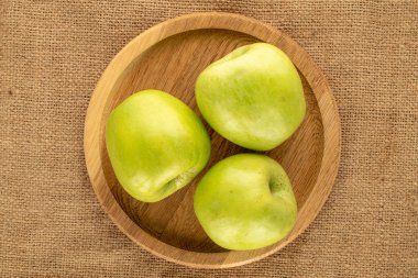 Jüt kumaş üzerinde bambu tabağı olan birkaç tane yeşil elma, yakın plan, üst manzara..