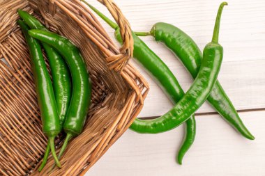 Biraz olgun organik, baharatlı yeşil acı biber, yakın plan, hasır sepetli, boyalı ahşap bir masa üzerinde..