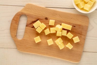 Tahta bir masa, makro, üst manzara üzerinde ahşap bir mutfak tahtasıyla küp şeklinde kesilmiş mis kokulu sert peynir..