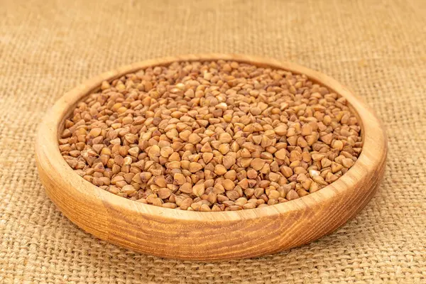 Ahşap bir tabakta çiğ karabuğday, jüt kumaş, makro.