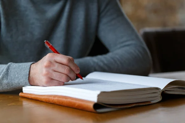 Business man in casual clothes writing with red pen in a journal