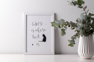 Seramik vazoda okaliptüs buketi ve gri duvarın üzerindeki boş resim çerçevesi, minimalist iç tasarım.