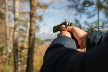 Beyaz bir adam yeşil bir ormanın arka planında elinde siyah bir polis tabancası tutuyor. İlk kişiden silah omuza.. 
