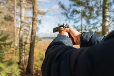 Beyaz bir adam yeşil bir ormanın arka planında elinde siyah bir polis tabancası tutuyor. İlk kişiden silah omuza.. 