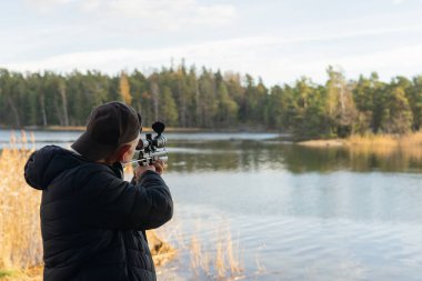 Elinde silah olan siyah ceketli bir adam gölün arka planına nişan alır..