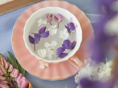 Suda yüzen küçük leylak ve lupin çiçekli porselen bardak. Klasik natürmort, üst görünüm.