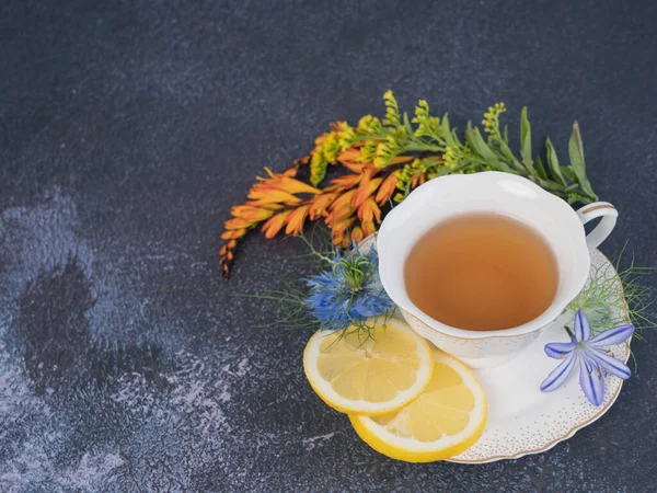 Tea time. An orange flower and a cup of black tea with lemon on a gray background. Top view. Space for text.
