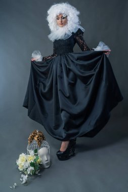 Klasik siyah elbiseli, beyaz yakalı ve gür kıvırcık peruklu güzel bir kız stüdyoda poz veriyor. Karnaval kostümü.