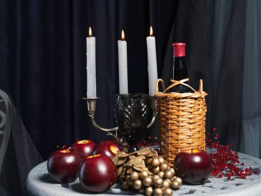 Dekoratif bir hayat yanan mumlar, hasır bir şarap şişesi, kırmızı elmalar ve koyu mavi arka planda altın bir şarap bahçesi..