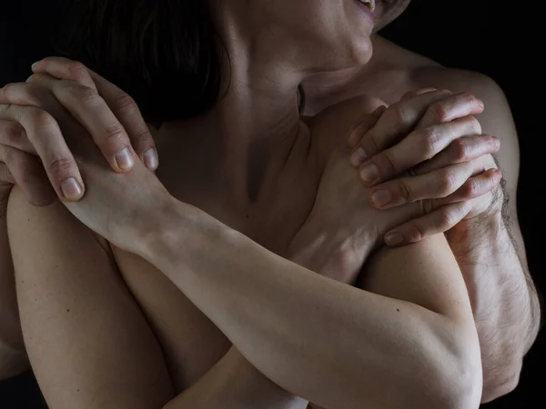 stock image A man hugs a woman from behind. Naked bodies. Plexus of the hands. Close-up photo without a face on a dark background.
