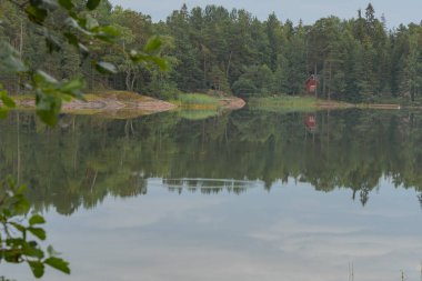 Sahilde ağaçlarla çevrili küçük kırmızı bir evi olan sessiz bir göl manzarası. İskandinavya. Doğal arkaplan.