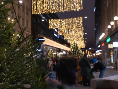 Helsinki, Finlandiya - 11 / 19 / 2022: Arka planda Helsinki 'nin merkez caddelerinde Noel süslemeleri ve aydınlatma odak dışı. Ön plandaki Noel ağacının dalları odaklanmış durumda..