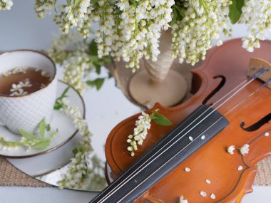 Bir buket kuş kirazı, bir fincan çay ve bir kemanla sanatsal bir hayat. Yatay fotoğraf.