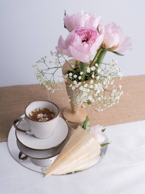 Bir buket pembe şakayık ve bir fincan çayla sanatsal bir hayat. Boynuzlu pembe şakayık çiçeği. Tasarım için çiçekler. Dikey fotoğraf.